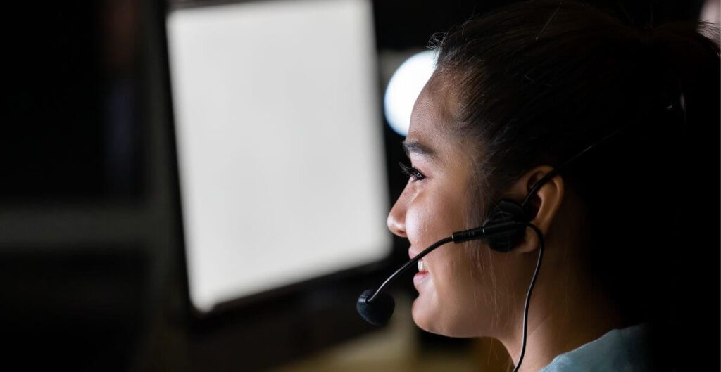 An outbound call centre agent smiling while facing a computer with headphones on