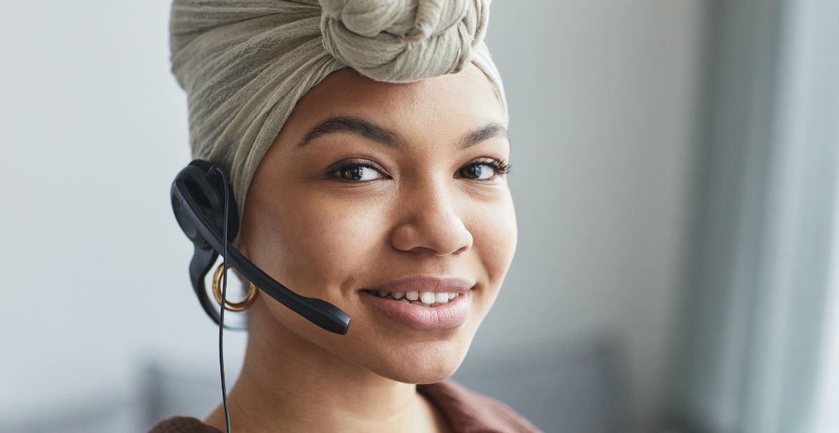 Who is a contact centre agent? | An African female contact centre agent, smiling brightly with a scarf tied around her head