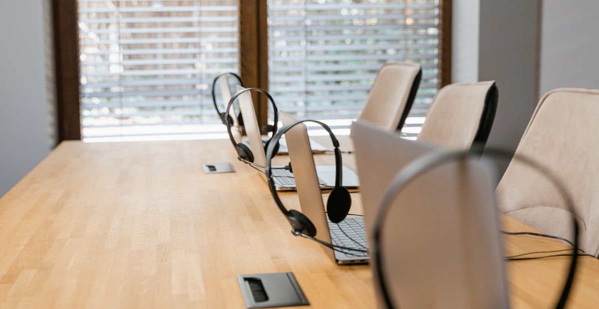 How to reduce employee turnover in a contact centre | Four headsets on four laptops seated on a big table in a contact centre