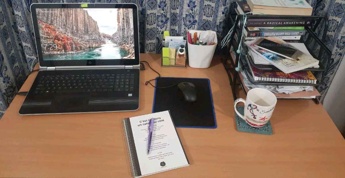 A laptop and a heap of books, a cup, book and pen in a remote workspace