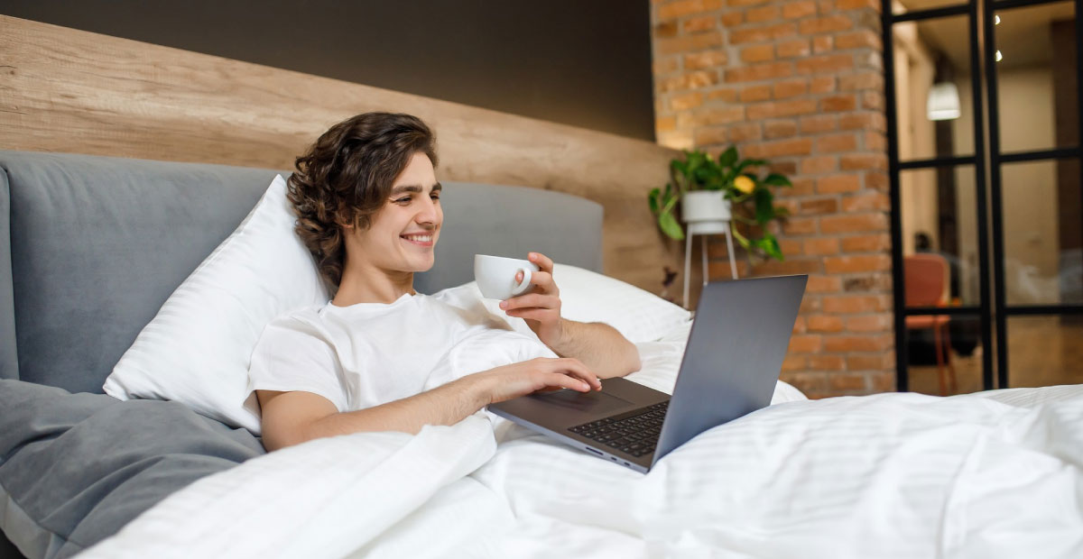 How important are extra amenities? | A  hotel guest enjoying acup of coffee and using his laptop on a comfortable bed.